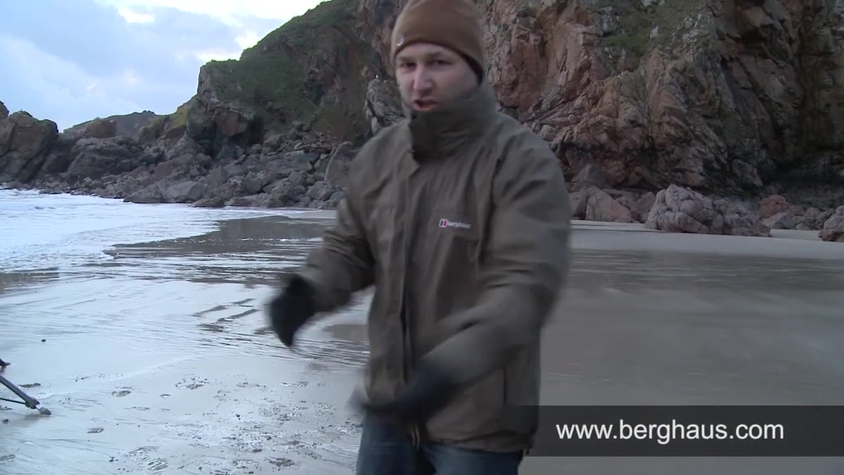Creator gesturing to waterproof jacket while standing on coastal rocks